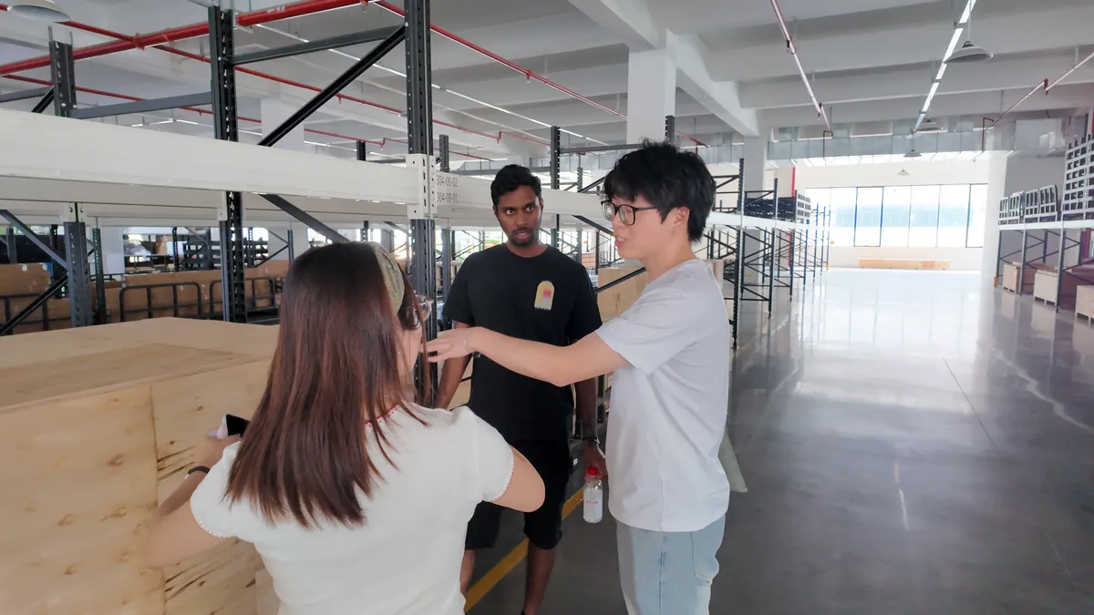 Several people walk through a large furniture workspace.
