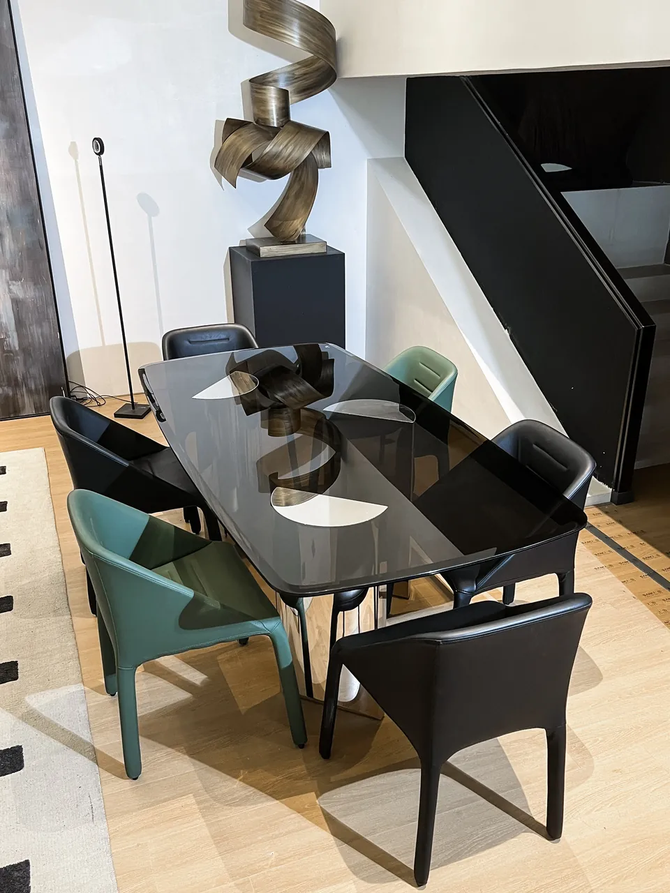 Dark rectangular tabletop with a slim reflective support, surrounded by six chairs in a furnished interior.