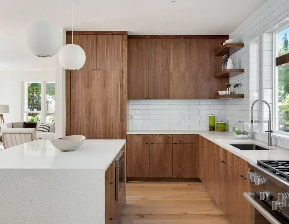 Pale kitchen island beside wood-toned floor-to-ceiling cabinetry and a white splashback.