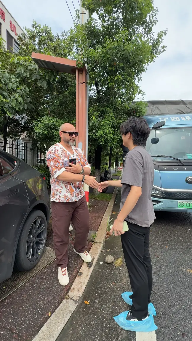 Two adults face one another with hands extended beside parked vehicles.