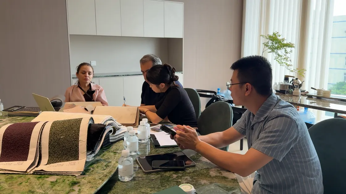 Four adults gather at a table with large fabric sample books, a laptop and phones.