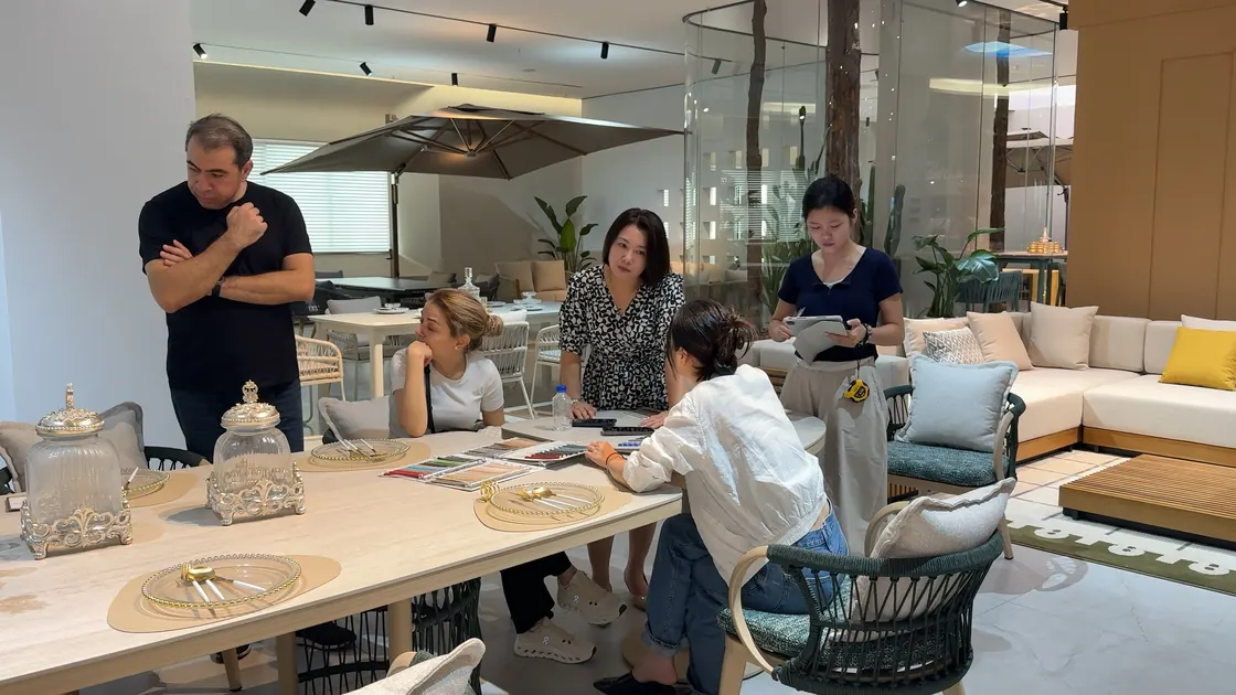 Five adults gather around a table with open fabric sample books.