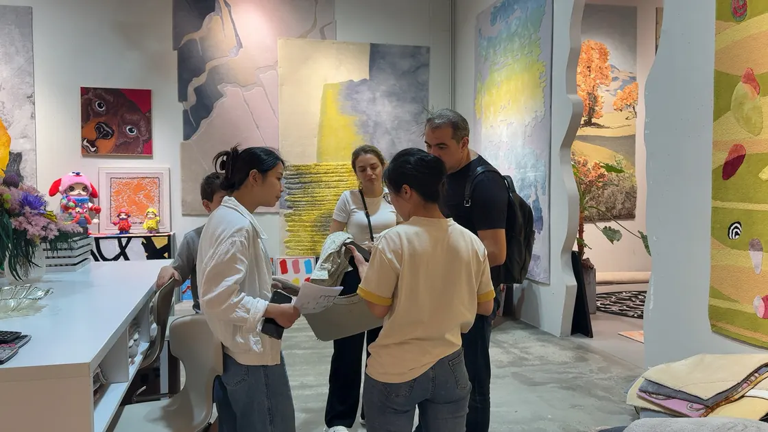 Adults hold and compare a rug sample in a showroom with colourful rugs on the walls.