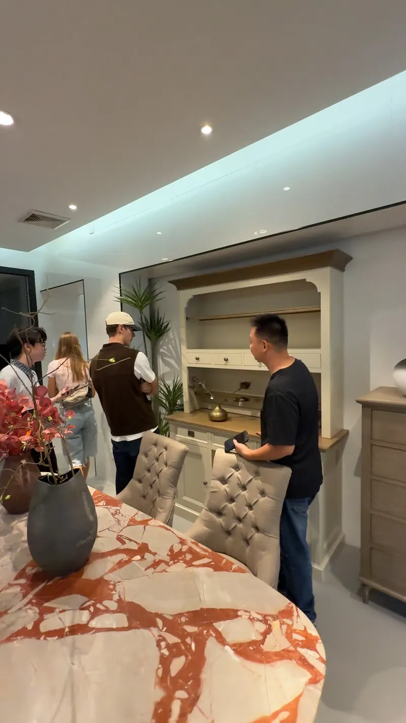 People stand beside a dining table and a wall cabinet display in a showroom.